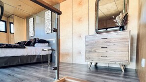 Une chambre à coucher moderne avec un plancher en bois, un lit doté d’une tête de lit, une commode et un miroir.