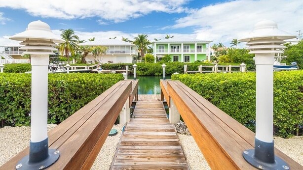 A wooden pathway leading to a building with a green facade, surrounded by greenery and a clear sky. - Key Colony Beach Paradise (Key Colony Beach)
