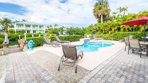 A pool area with lounge chairs, a red umbrella, and a view of a building in the background. - Key Colony Beach Paradise (Key Colony Beach)