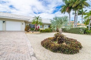 Il s’agit d’une propriété résidentielle dotée d’une allée pavée, d’un garage et d’un jardin aménagé avec des palmiers et des arbustes.