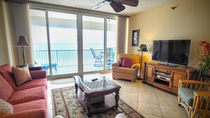 Un salon comprenant un canapé, des fauteuils, une table basse, un téléviseur et un balcon avec vue.
