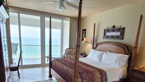 Un lit à baldaquin avec une couvre-lit à motifs, un ventilateur de plafond, une vue sur le balcon et une citation encadrée accrochée au mur.