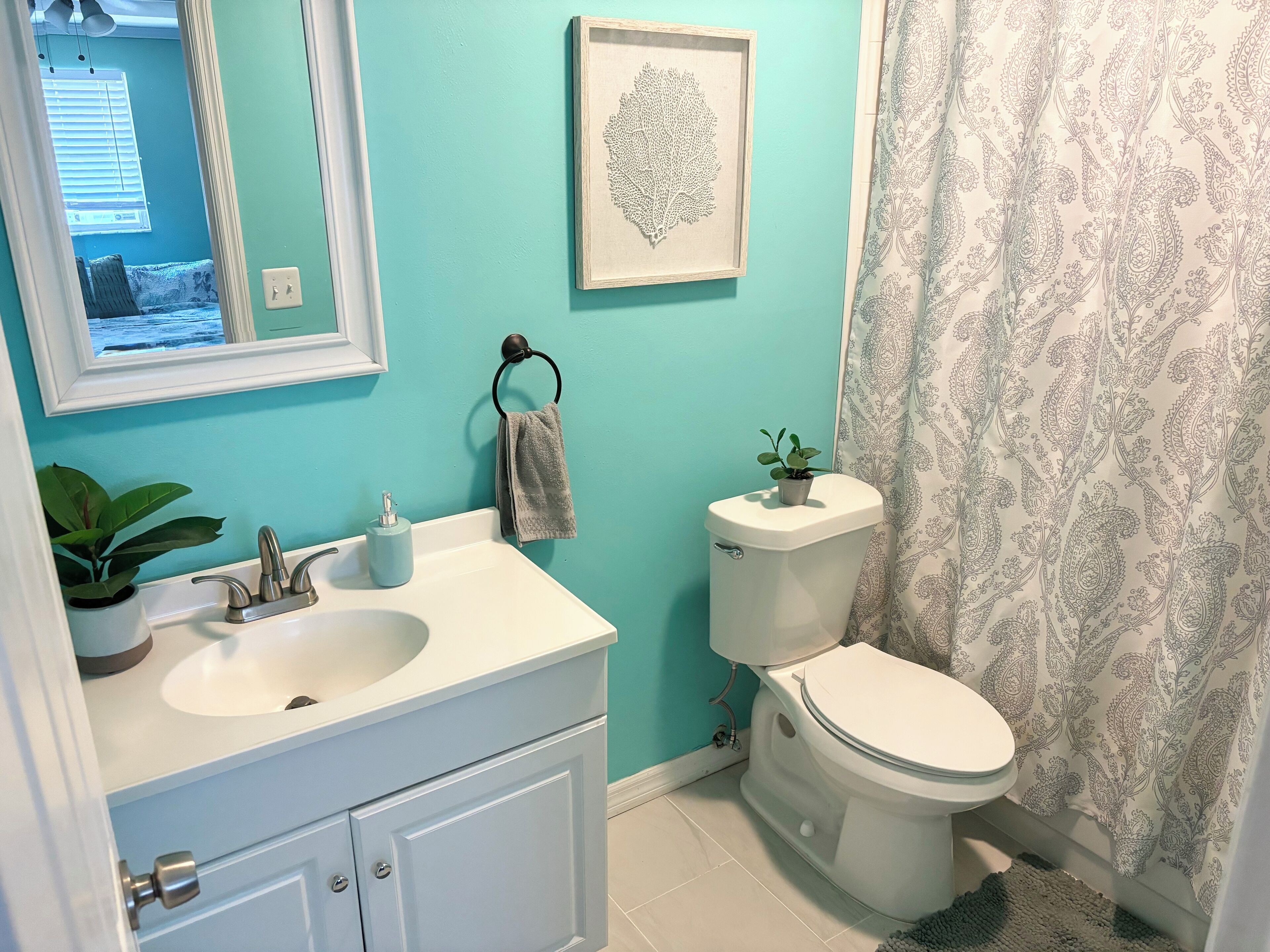 A bathroom with a sink, toilet, and a framed artwork on the wall.