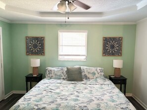 Un dormitorio con una cama, dos mesitas de noche, dos lámparas de pared, un ventilador de techo y dos elementos decorativos en la pared.