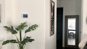Un couloir doté d’un parquet en bois foncé, de murs blancs, d’une plante en pot, d’une œuvre d’art encadrée et d’une porte donnant sur une autre pièce.