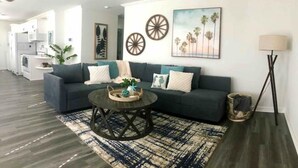 Un salon avec un canapé vert foncé, une table basse ronde et un tapis à motifs. On y trouve également des décorations murales, une lampe et une plante.