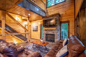 Cozy living area with a stone fireplace, comfortable seating, and a staircase leading to an upper level.