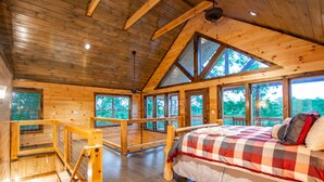 Quarto de cabana de madeira com cama, janelas amplas e varanda.