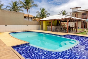 Une piscine aux carreaux bleus, un patio couvert et des palmiers.