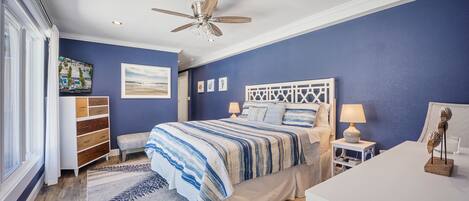 Un dormitorio con cama, mesitas de noche, ventilador de techo y obras de arte en las paredes.