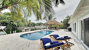 A swimming pool with lounge chairs, a thatched-roof structure, and a view of a marina. - Waterfront Oasis w/ Pool, Tiki Lounge, Dock & BBQ (Marathon)