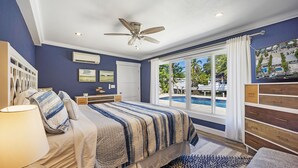 A bedroom with a large bed, a ceiling fan, a window with a view of a swimming pool, and a nightstand with a lamp. - Waterfront Oasis w/ Pool, Tiki Lounge, Dock & BBQ (Marathon)