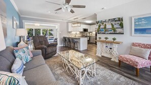 A modern living room with a glass coffee table, a sofa, and a chair. There is a kitchen area with a bar and a dining table. - Waterfront Oasis w/ Pool, Tiki Lounge, Dock & BBQ (Marathon)