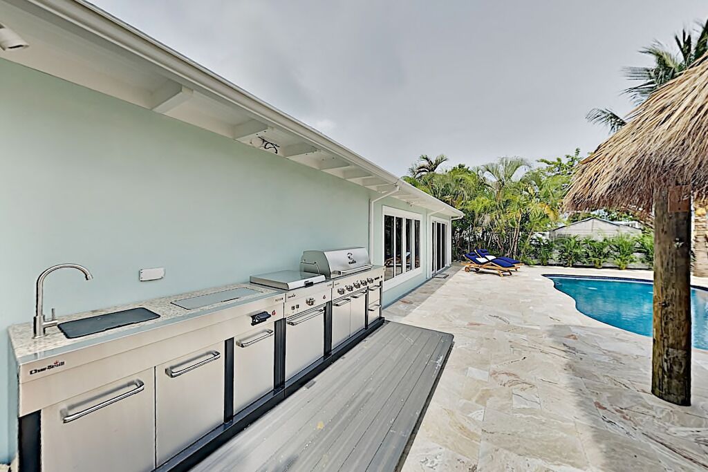 A modern outdoor kitchen with a built-in sink and grill, adjacent to a swimming pool with lounge chairs.