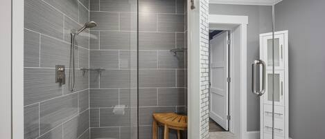A modern bathroom with a glass-enclosed shower, a wooden chair, and a white cabinet.