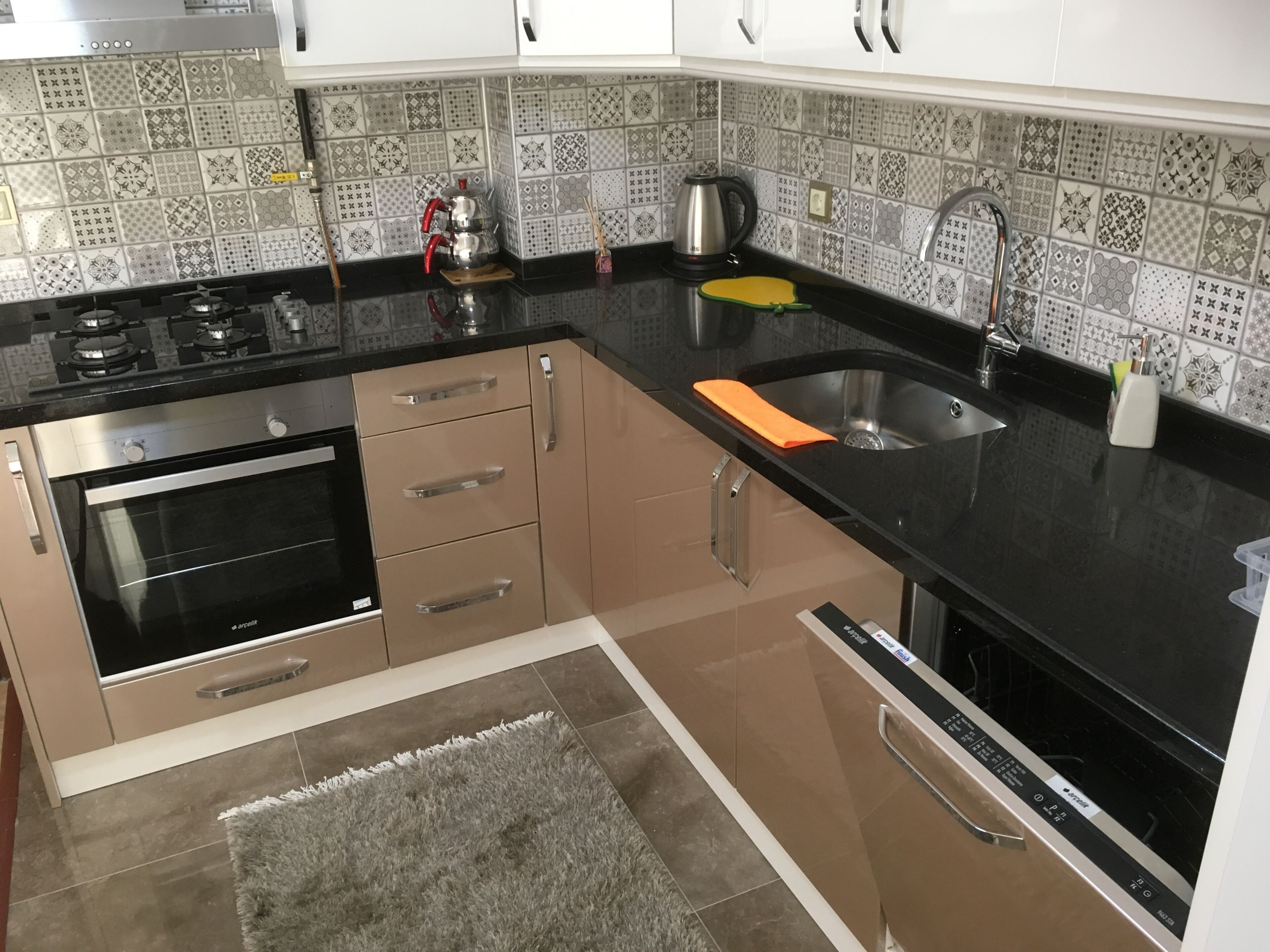 A kitchen with a stove, oven, sink, and patterned backsplash.