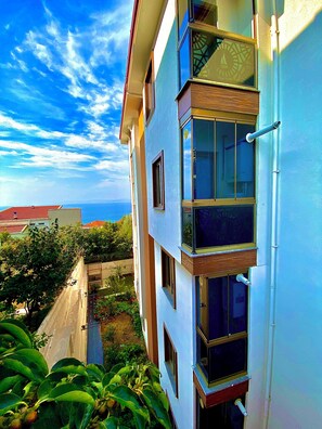 A multi-story building with balconies, large windows, and a view of the sea.