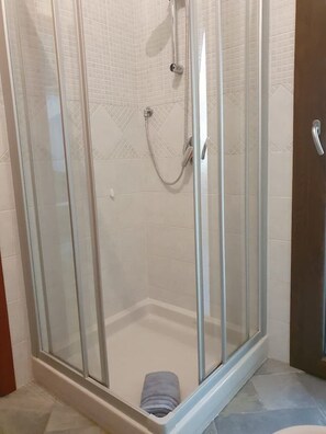 A glass-enclosed shower with a handheld showerhead and a towel on the floor.