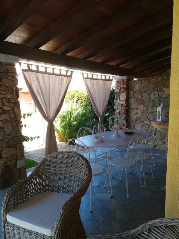 An outdoor patio with a stone wall, a round table, and wicker chairs.
