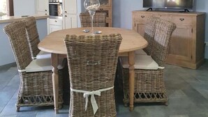 A dining area with a round table and wicker chairs, a television on a wooden cabinet, and a kitchen in the background. - Cozy newly built cottage, within walking distance of the center. (VILLASIMIUS)