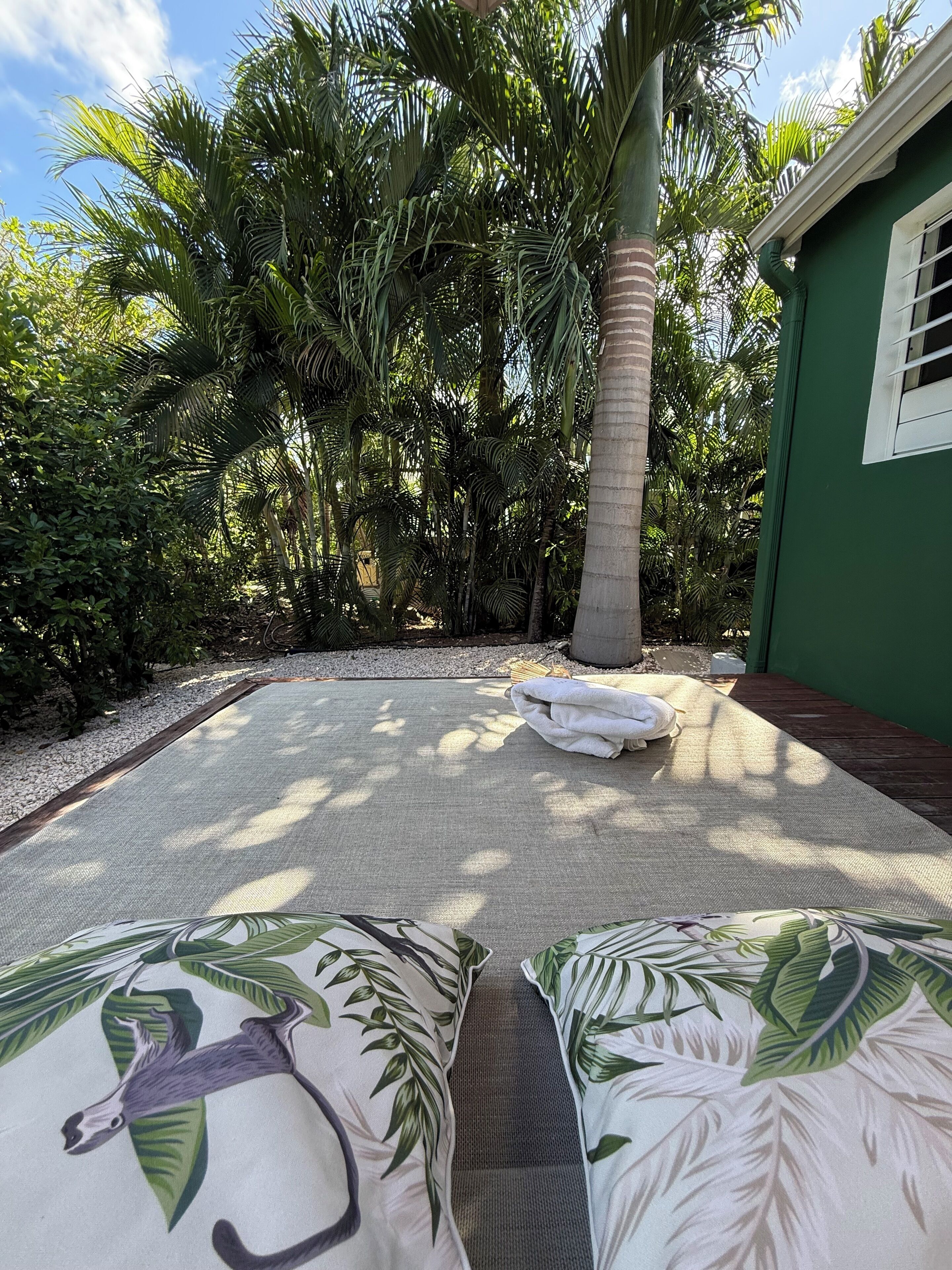 Een kamer met een groot bed, een groene wand en uitzicht op een weelderige tuin met palmbomen.