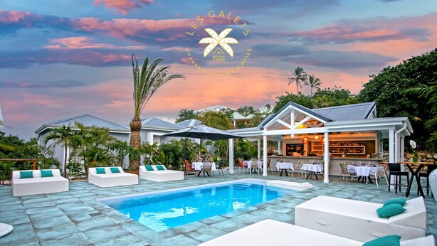A pool area with white lounge chairs and a bar. - Les Galets Sxm (Orient Bay)