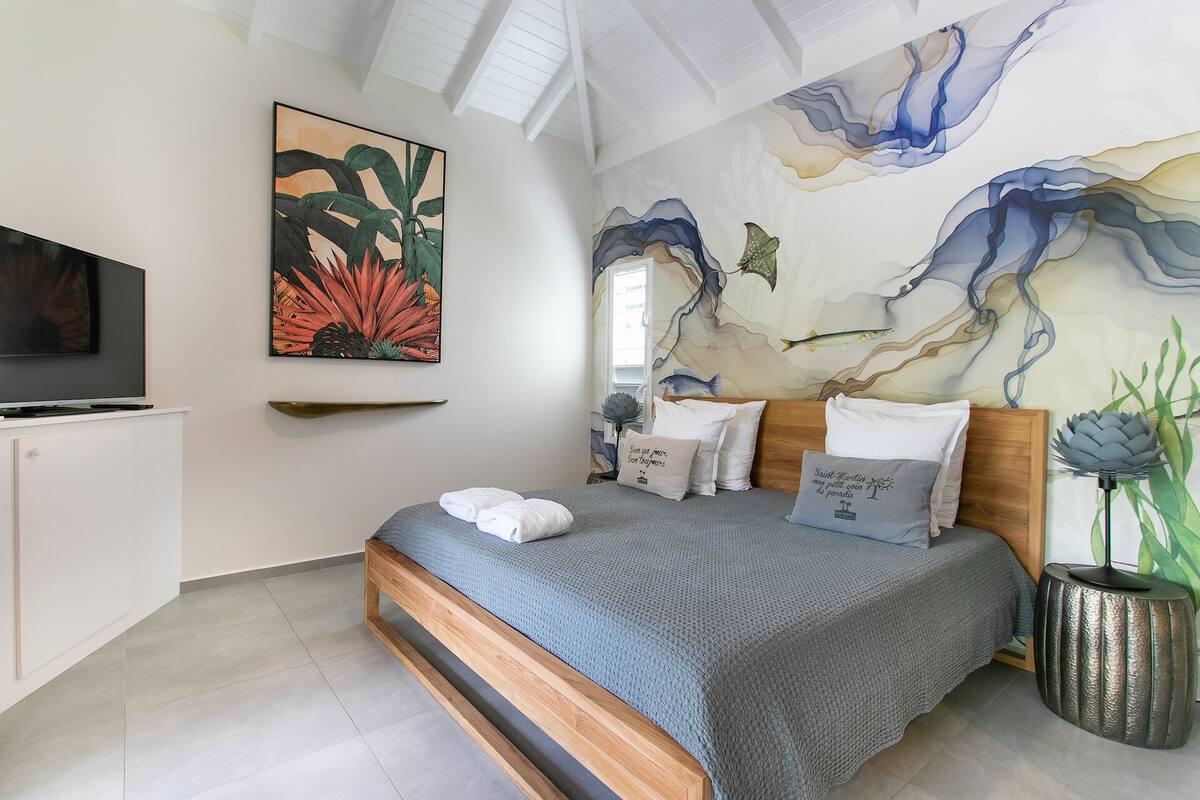 A modern bedroom with a large bed, a flat-screen TV, and a mural on the wall.