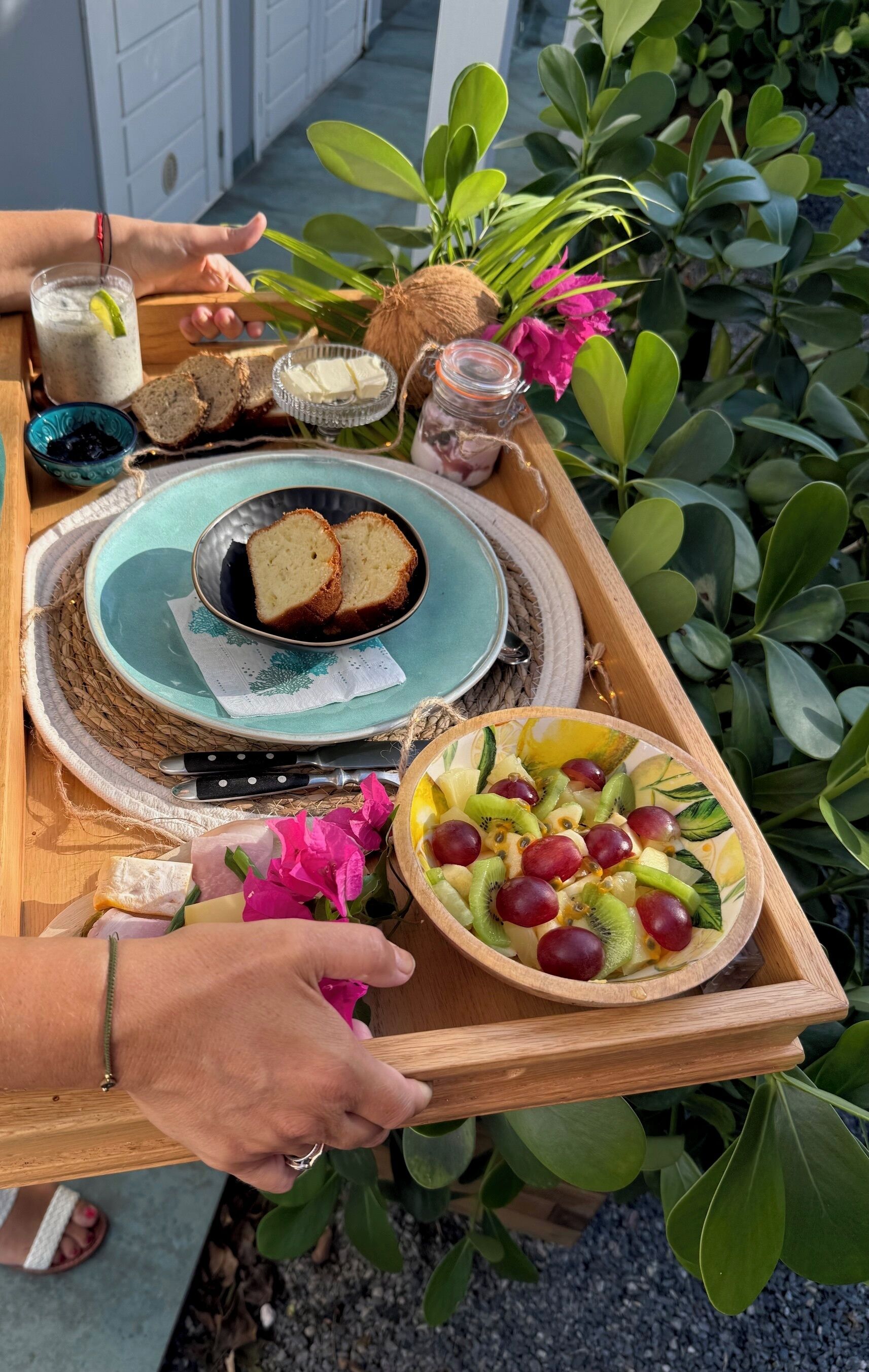 A wooden tray with a plate of bread, a bowl of fruit, and a glass of water.