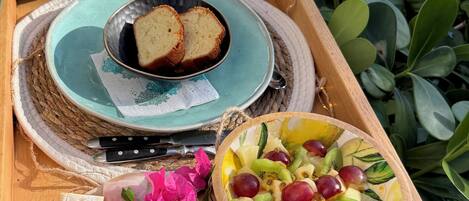A wooden tray with a plate of bread, a bowl of fruit, and a glass of water.