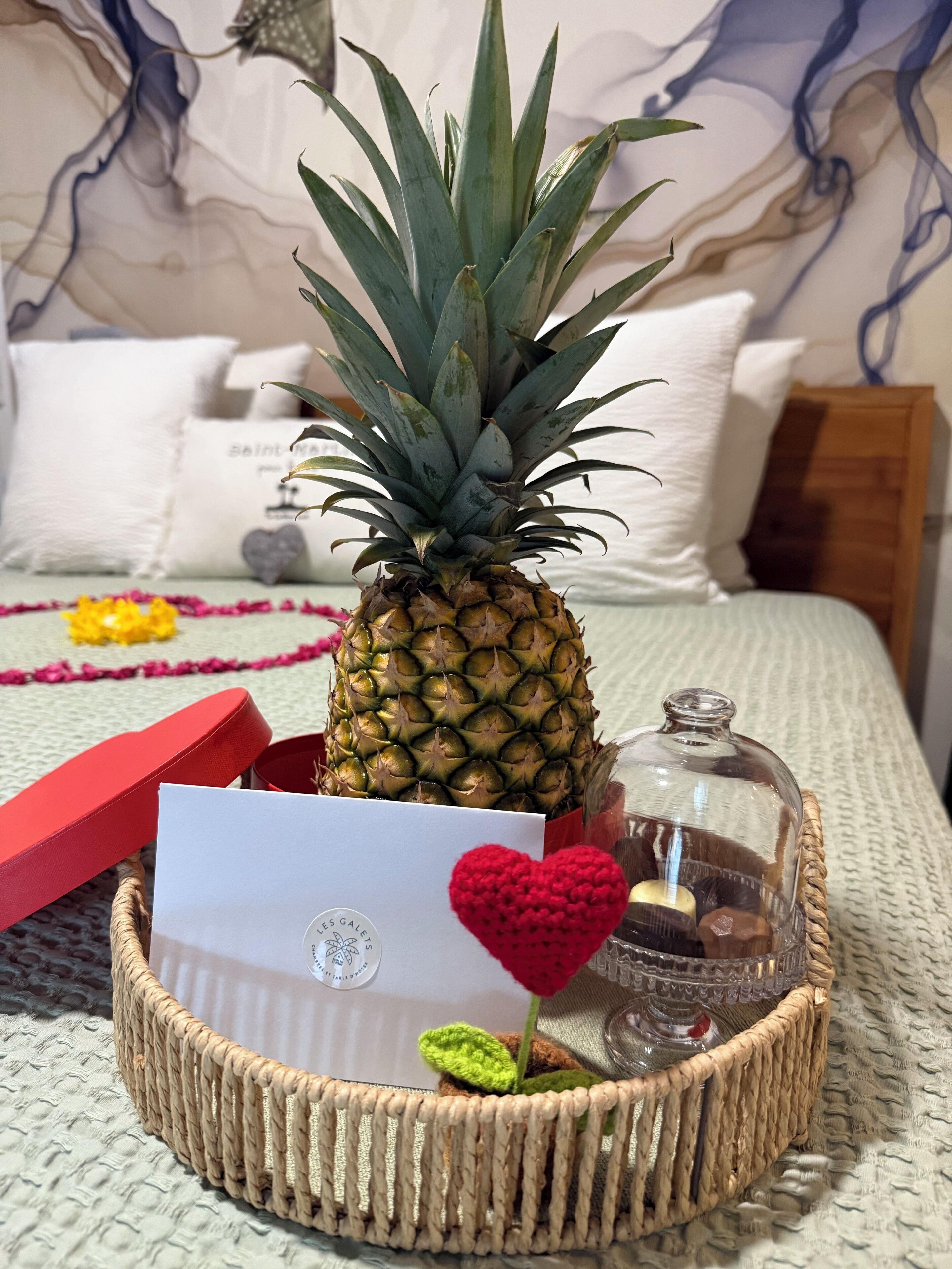 A pineapple on a bed with a card, a crocheted heart, and a glass jar.