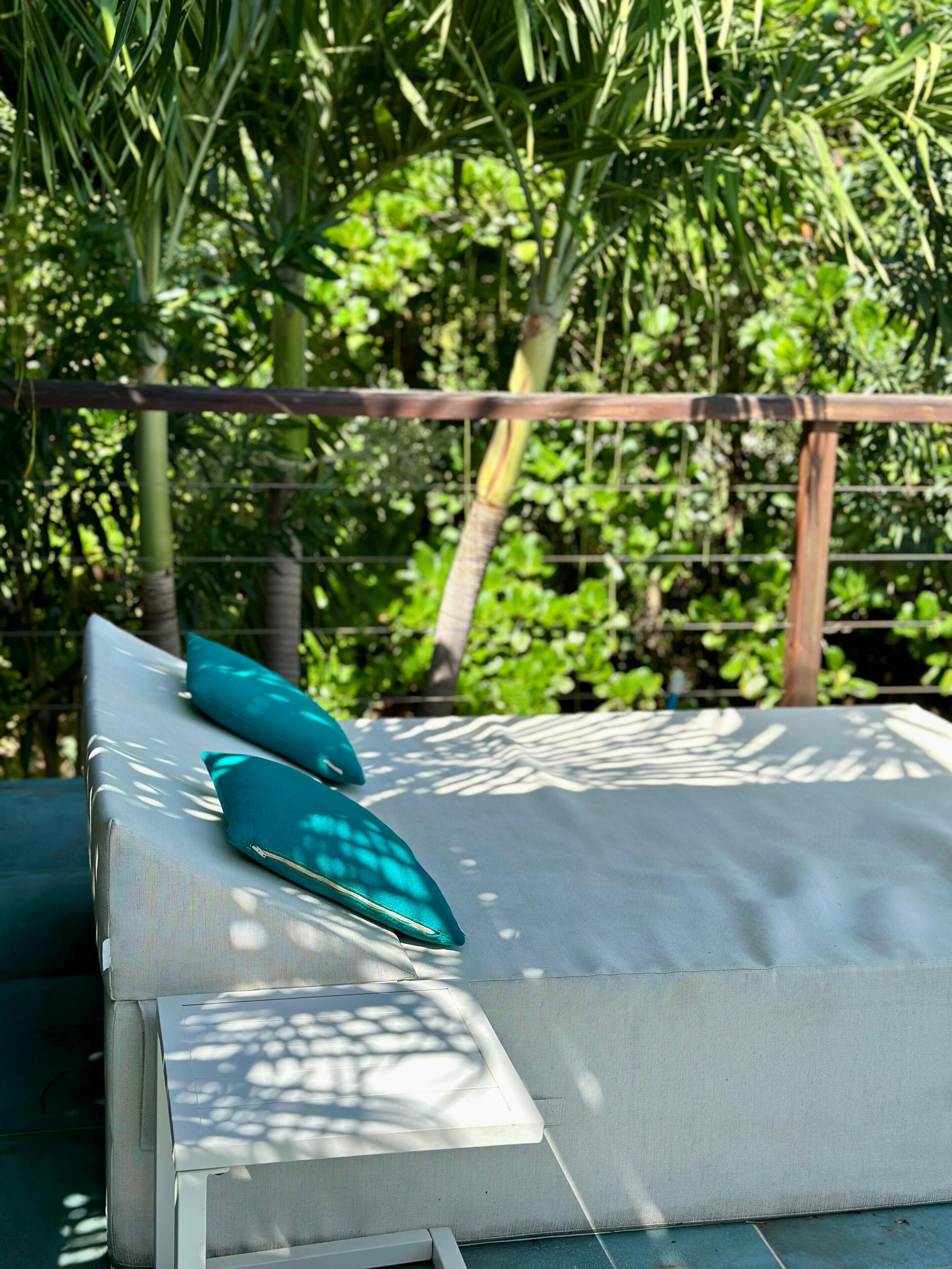 Un espace extérieur ensoleillé avec des sièges, comprenant un banc rembourré et deux coussins de couleur turquoise.