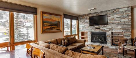 A cozy living room with a stone fireplace, a large TV mounted on the wall, and a comfortable seating area with a sofa and chairs.