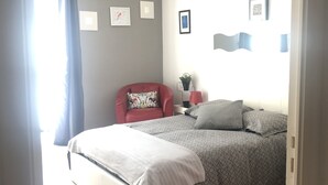 Une chambre à coucher avec un lit, une chaise rouge, une petite table et une fenêtre avec des rideaux.