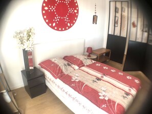 Une chambre à coucher avec un lit, une table de chevet, un vase de fleurs et un élément de décoration rouge sur le mur.