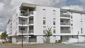 Un immeuble résidentiel moderne à plusieurs étages, doté de balcons, d’une entrée bien visible et donnant sur la rue.
