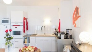 Une cuisine moderne avec des armoires blanches, un évier et un four à micro-ondes. Des serviettes rouges sont accrochées aux armoires, et un vase rempli de fleurs est posé sur le comptoir.