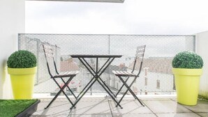 Un balcon avec une balustrade en métal, deux chaises, une petite table et deux plantes en pot.