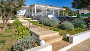 A modern house with a covered patio, a stone pathway, and a variety of plants. - Villa Abril - modern villa only 400 mts from beach (Binisafua)