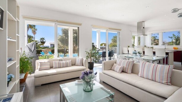 A spacious living area with a sofa set, a glass coffee table, and a view of a pool and garden. - Villa Abril - modern villa only 400 mts from beach (Binisafua)