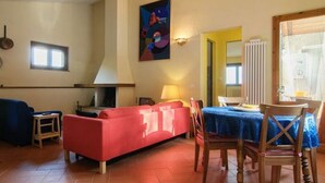 A living room with a red sofa, a dining table with chairs, a lamp, and a painting on the wall. - Il ponticello Cortona, delightful little house in the green with breathtaking views (Cortona)