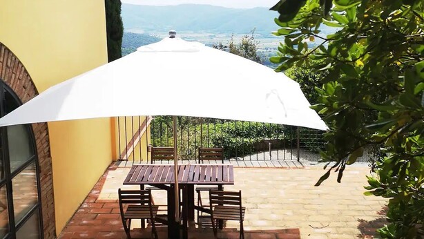 A patio with a table and chairs under a white umbrella, overlooking a scenic view. - Il ponticello Cortona, delightful little house in the green with breathtaking views (Cortona)