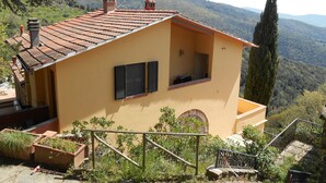 A yellow building with a tiled roof, a small balcony, and a view of a forested mountain range. - Il ponticello Cortona, delightful little house in the green with breathtaking views (Cortona)