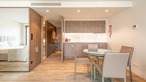 Una habitación de hotel moderna con una cama grande, una sala de estar separada con un sofá y una mesa de comedor con sillas.