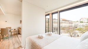 Habitación de hotel moderna con una cama grande, un escritorio y vistas de la ciudad a través de amplios ventanales.