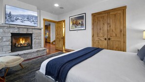 Une chambre avec une cheminée en pierre, des portes en bois et un lit recouvert d’une couverture bleue.