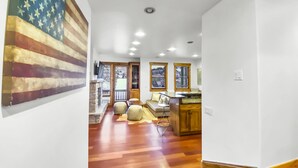 Un vaste espace de vie doté d’un plancher en bois, d’une cheminée en pierre, d’un grand drapeau américain et d’un coin cuisine avec des armoires en bois et un comptoir.
