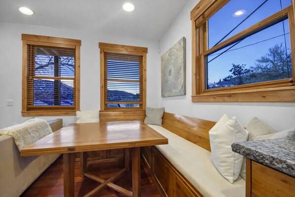 A cozy room with a wooden table, bench seating, and large windows with wooden frames.