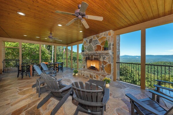An outdoor patio with stone flooring, Adirondack chairs, a stone fireplace, and a view of the landscape.