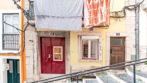Eine Treppe führt zu einem Gebäude mit nummerierten Türen, einem Fenster und einem Balkon mit Geländer.