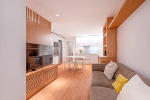 A modern kitchen with white cabinets, a dining area with a white table and chairs, and a grey sofa with yellow cushions.
